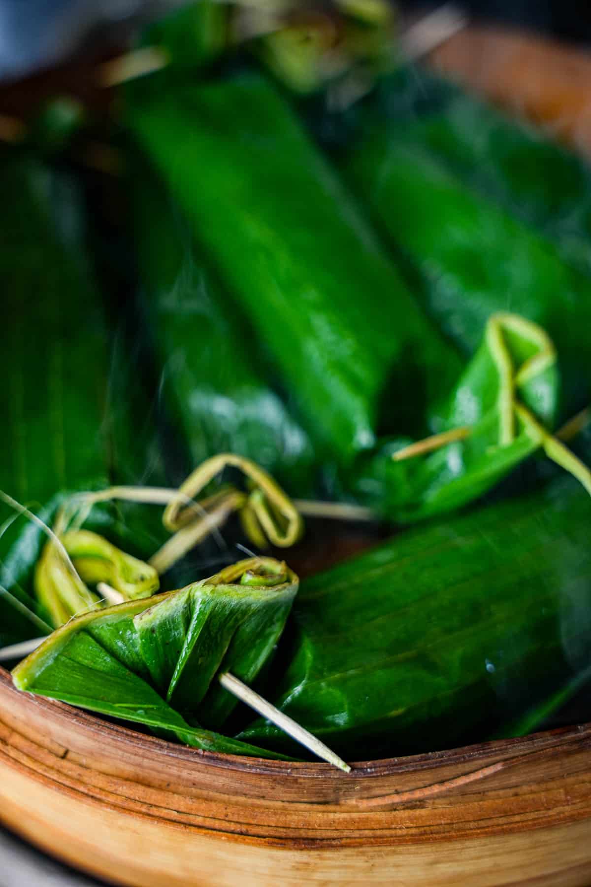 Steaming lontong in a bamboo steamer. You can see steam ricing up between the banana leaves.