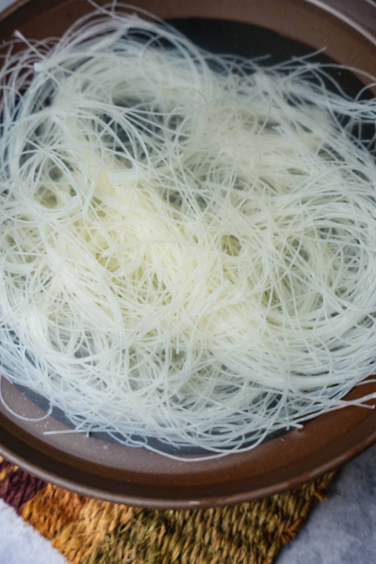 Rice noodles soaking in a bowl of water to rehydrate.