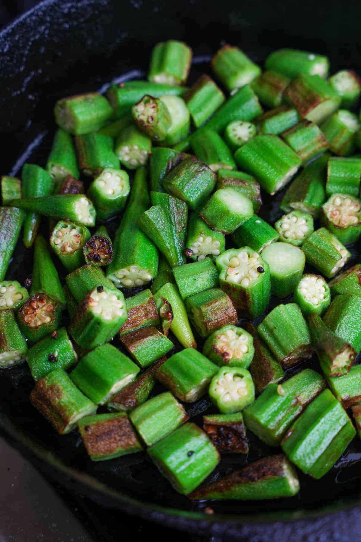 Vibrant green okra is pan fried in a cast iron skillet.