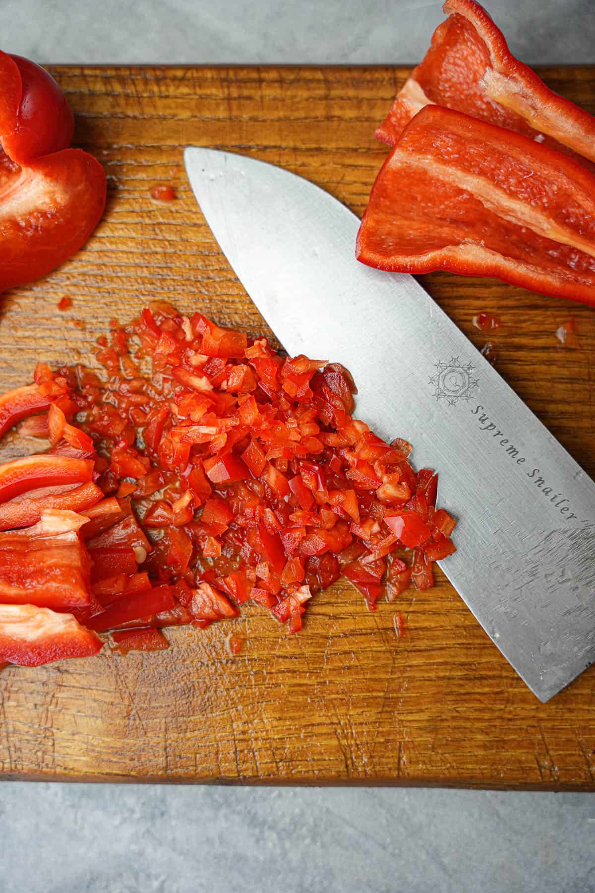 A sharp knife is mincing peppers on a wooden cutting board.