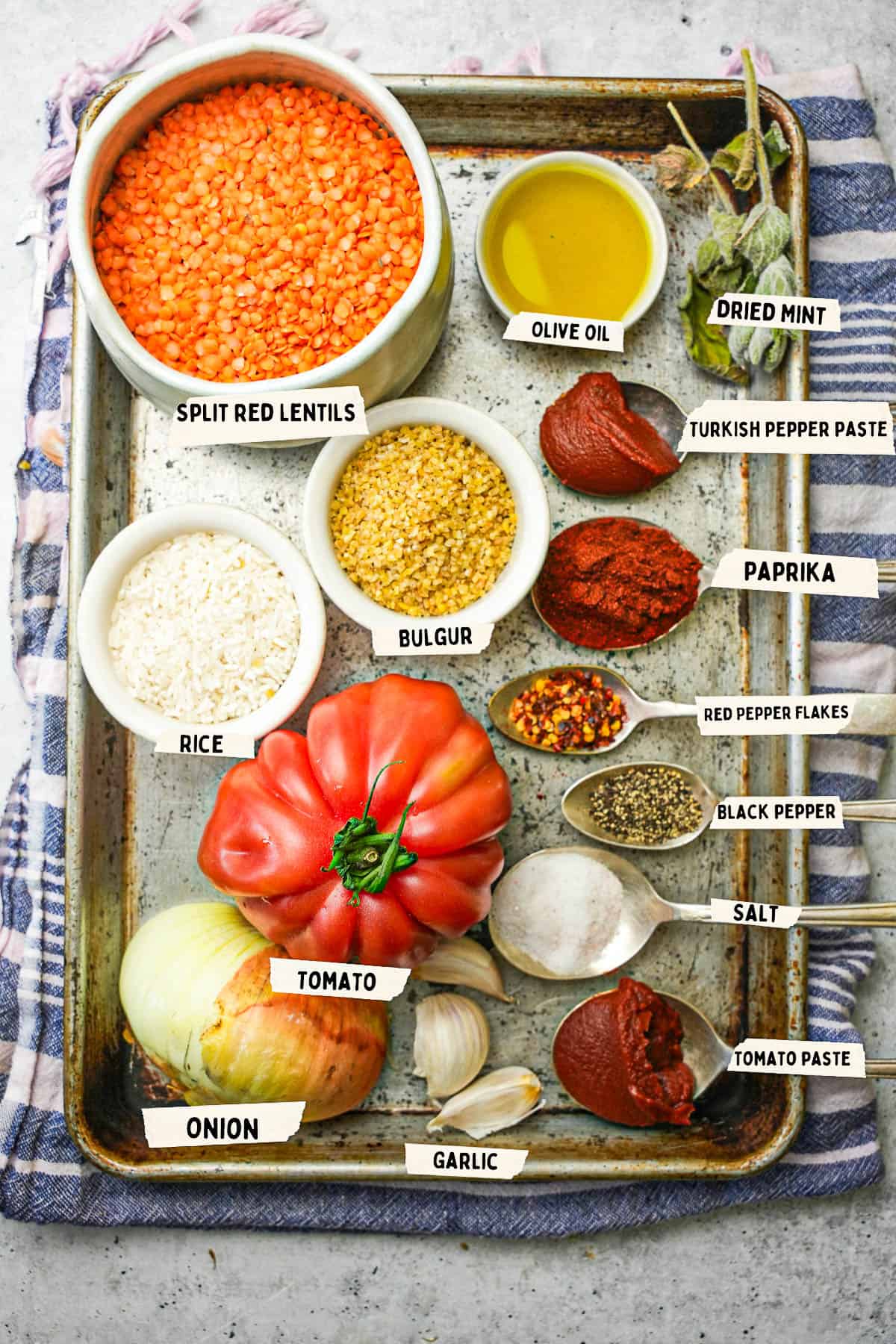 Ingredients for ezogelin measured out and labeled on a metal tray sitting on top of a blue striped cloth.