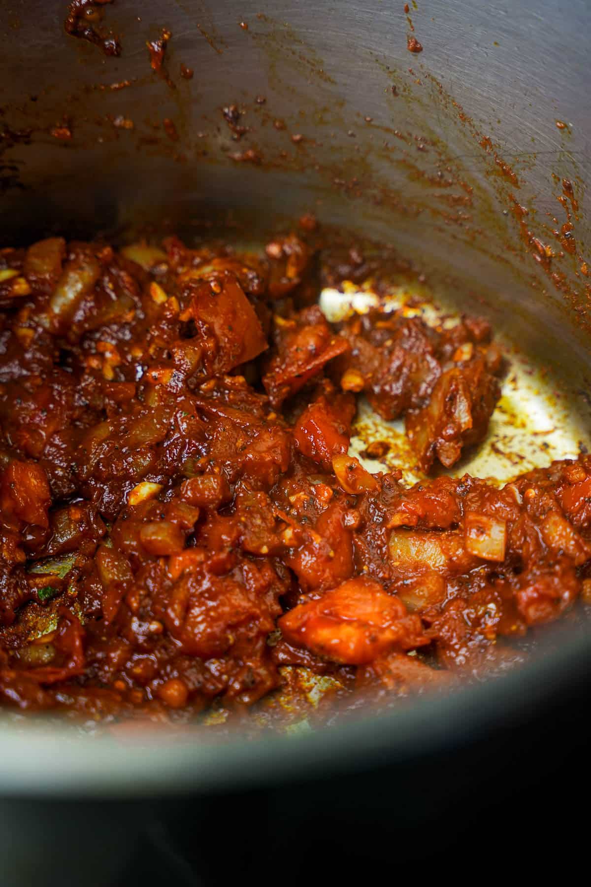 Tomatoes and seasonings are cooking down to for the base for the soup in a stainless steel pot.