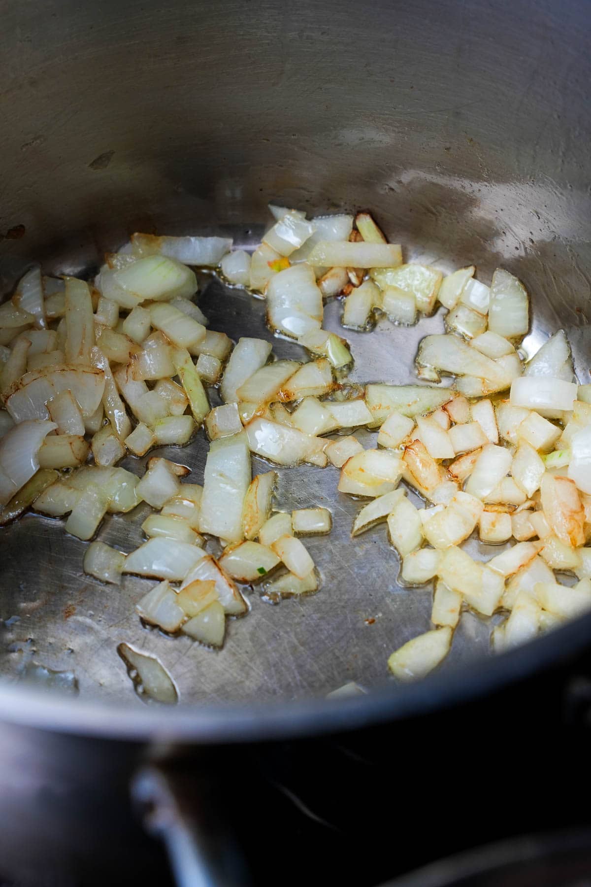 Onions sautéing in olive oil in a stainless steel pot.