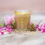 goma dressing in a glass jar surrounded by edible flowers and sesame seeds.
