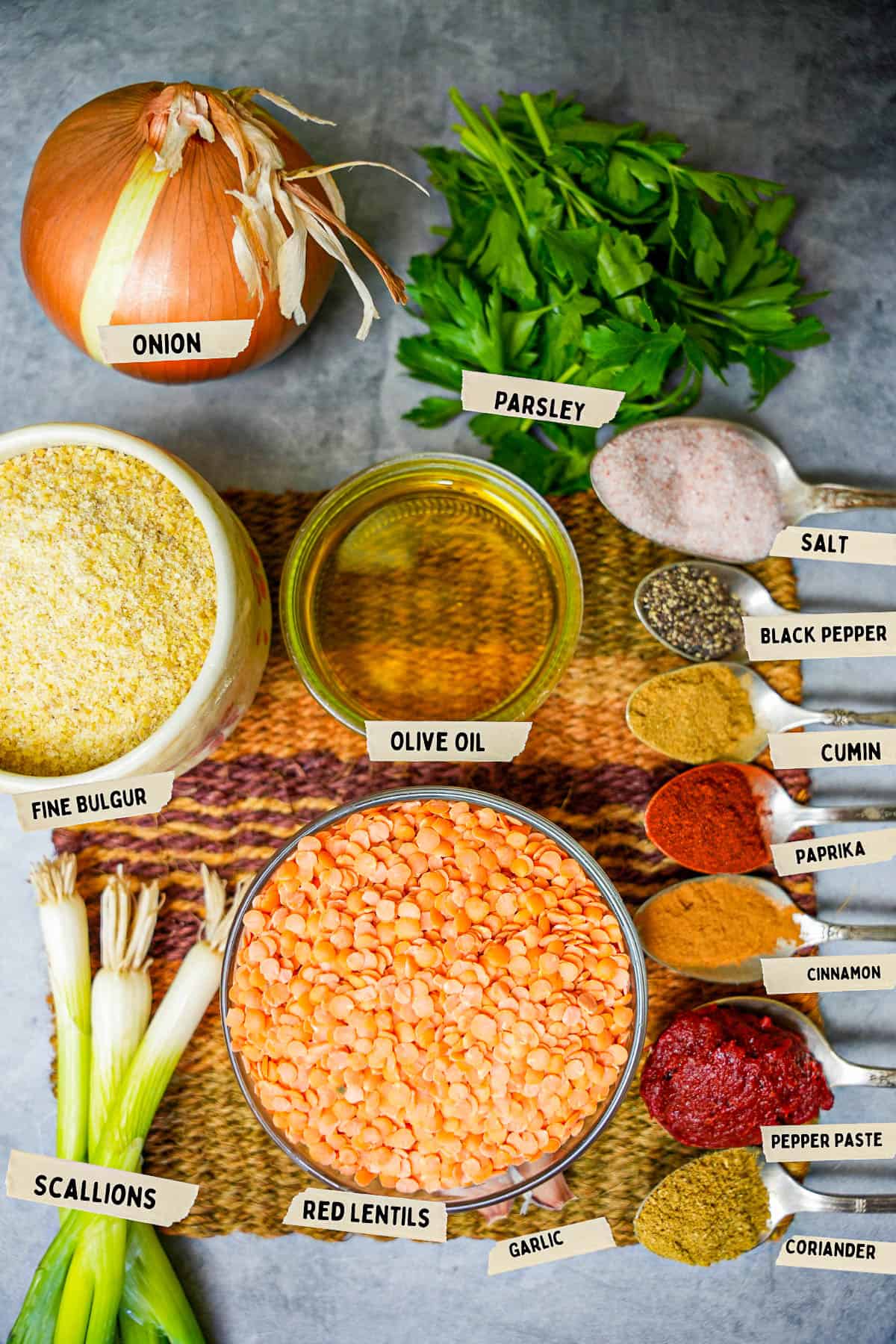 Mercimek kofte ingredients are laid out and labeled on a stone countertop. All spices are in little silver spoons.