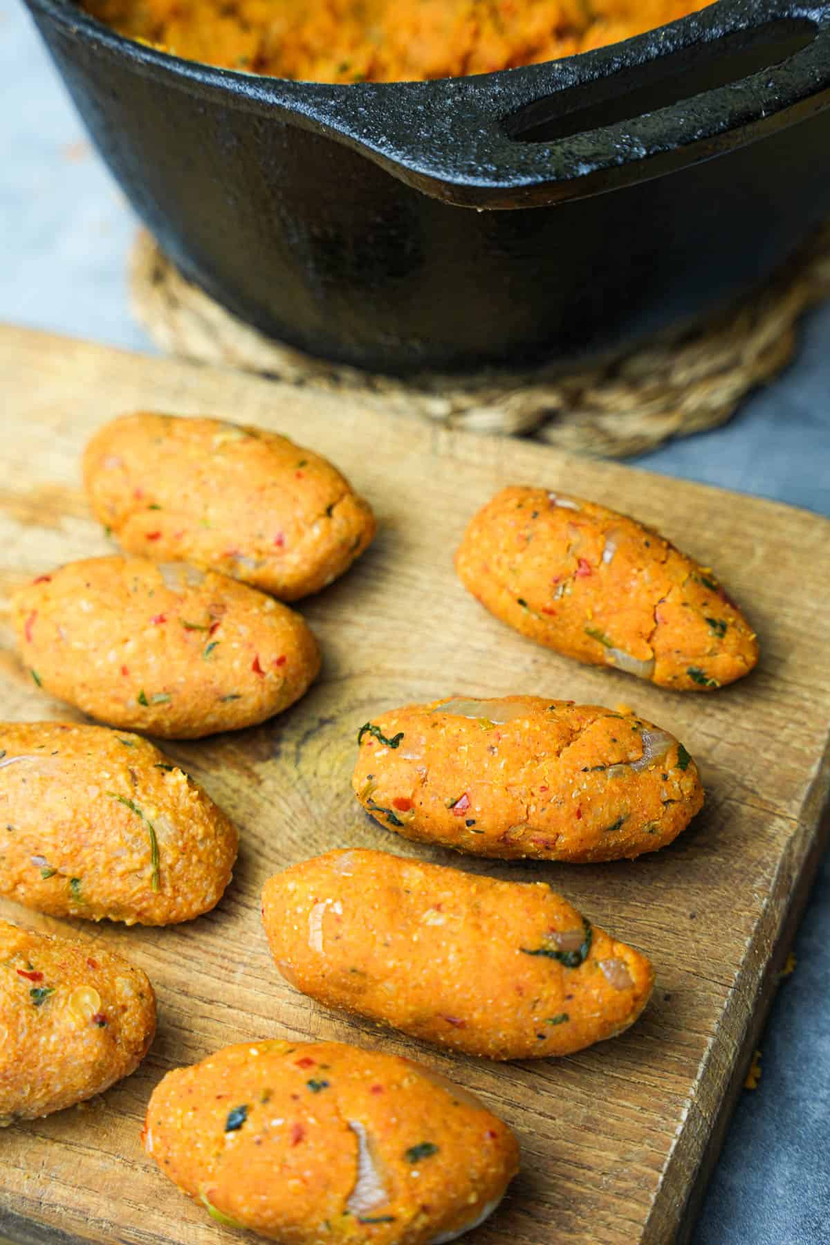 Kofte are formed by hand into oval shapes on a wooden board next to a black metal pot of the dough mixture.