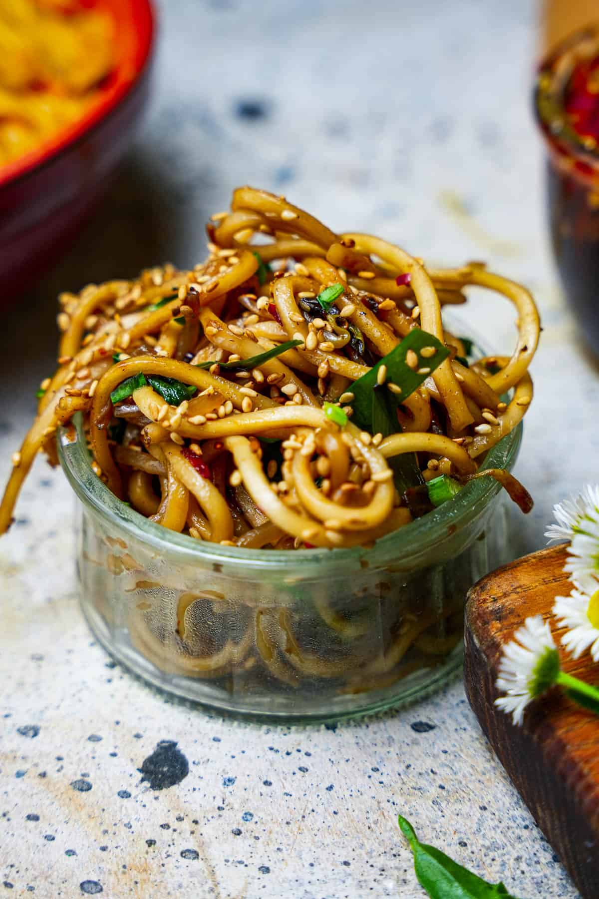 A small glass bowl with Mi Xao in it, garnished with sesame seeds and fresh chives.