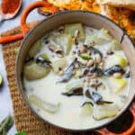An orange pot of olan on a woven mat with pickle, herbal garnishes, and grilled naan bread.