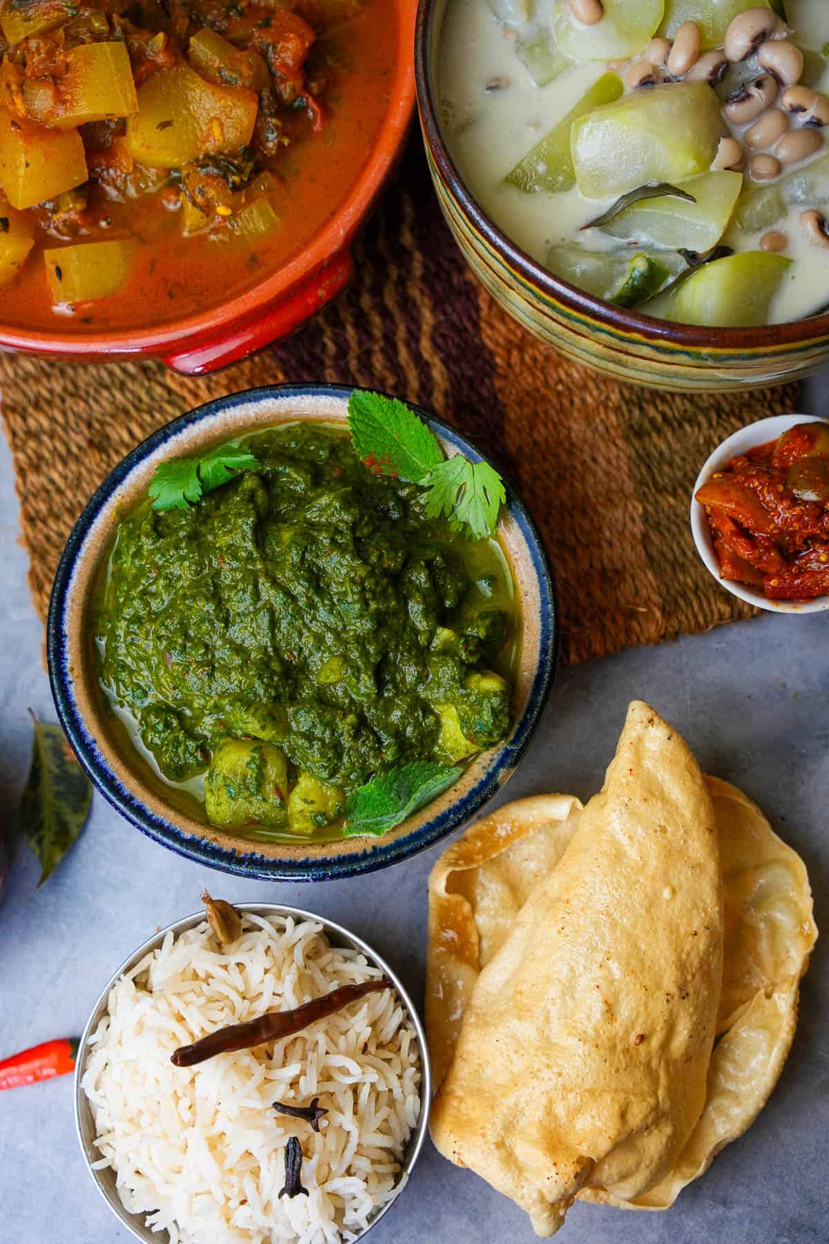 Saag aloo garnished with cilantro and mint leaves served alongside papad, basmati rice, pickle and sabjis.