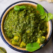 Saag aloo garnished with cilantro and mint leaves in a blue rimmed ceramic bowl.