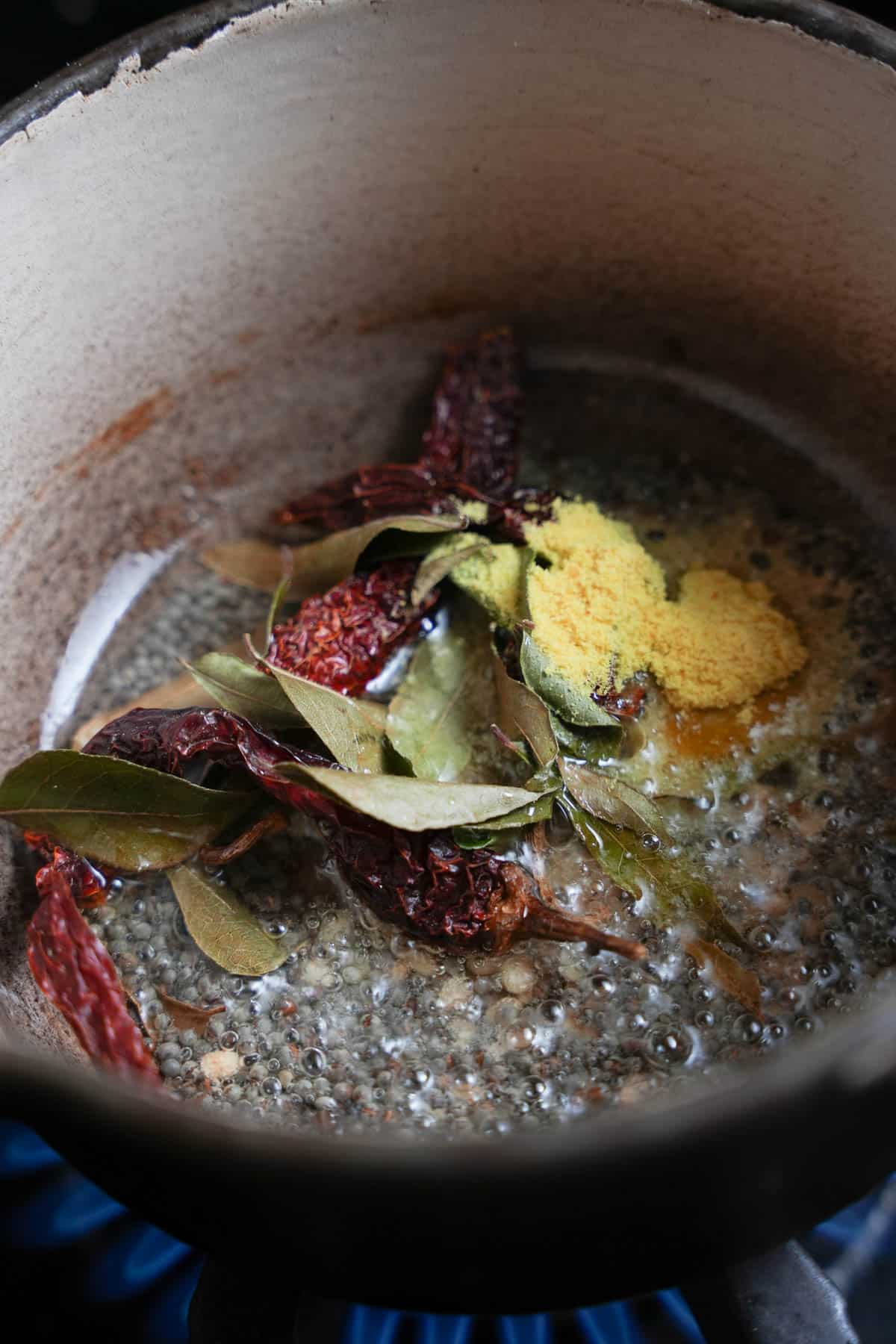 Curry leaves, dried chilies and hing are added to the frying mustard seeds and urad dal in a small pot.