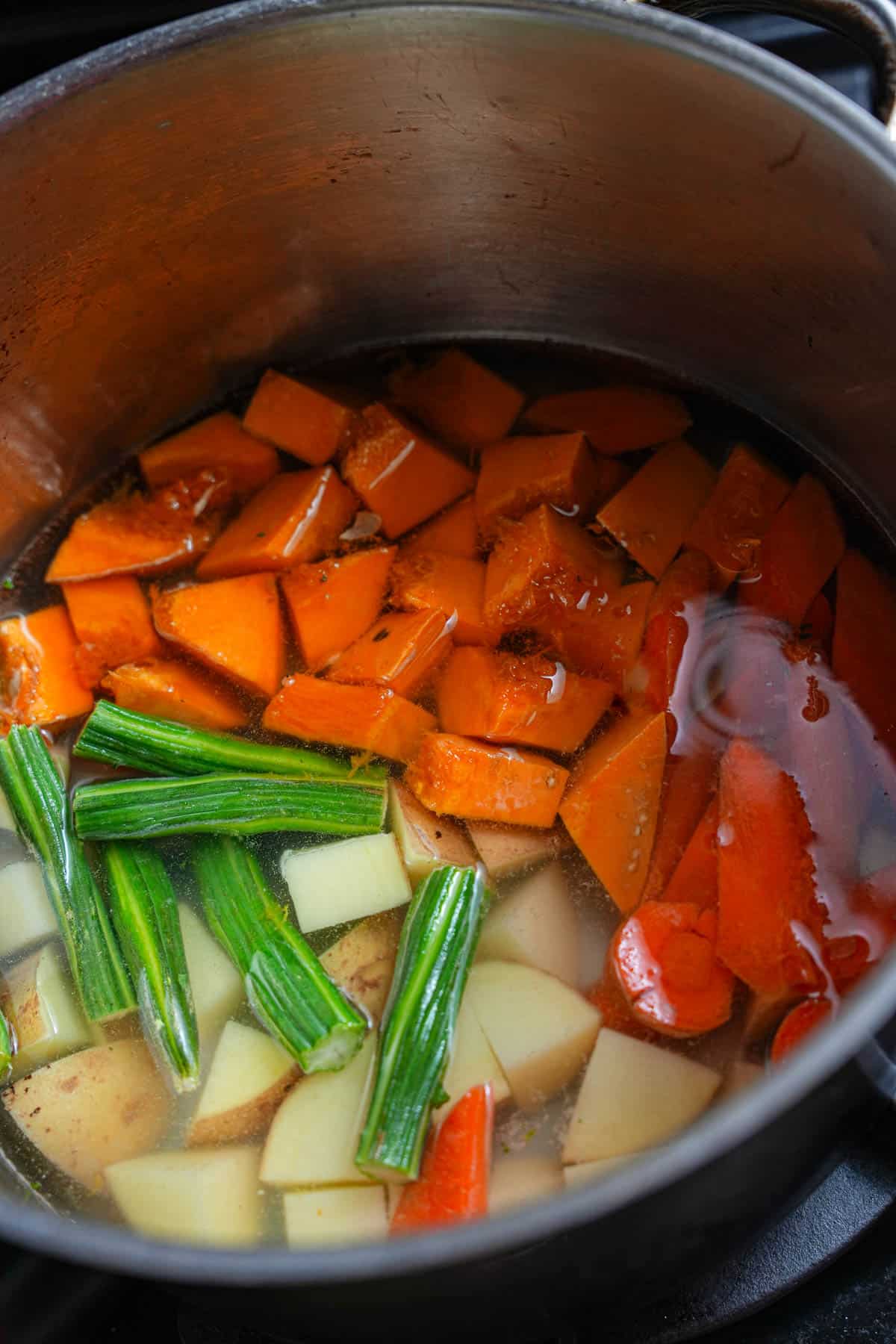 Pumpkin, moringa, potatoes, and carrot are brought up to a boil in a pot with water on the stove.