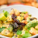 Aviyal garnished with tadka and cilantro leaves in a white ceramic bowl.