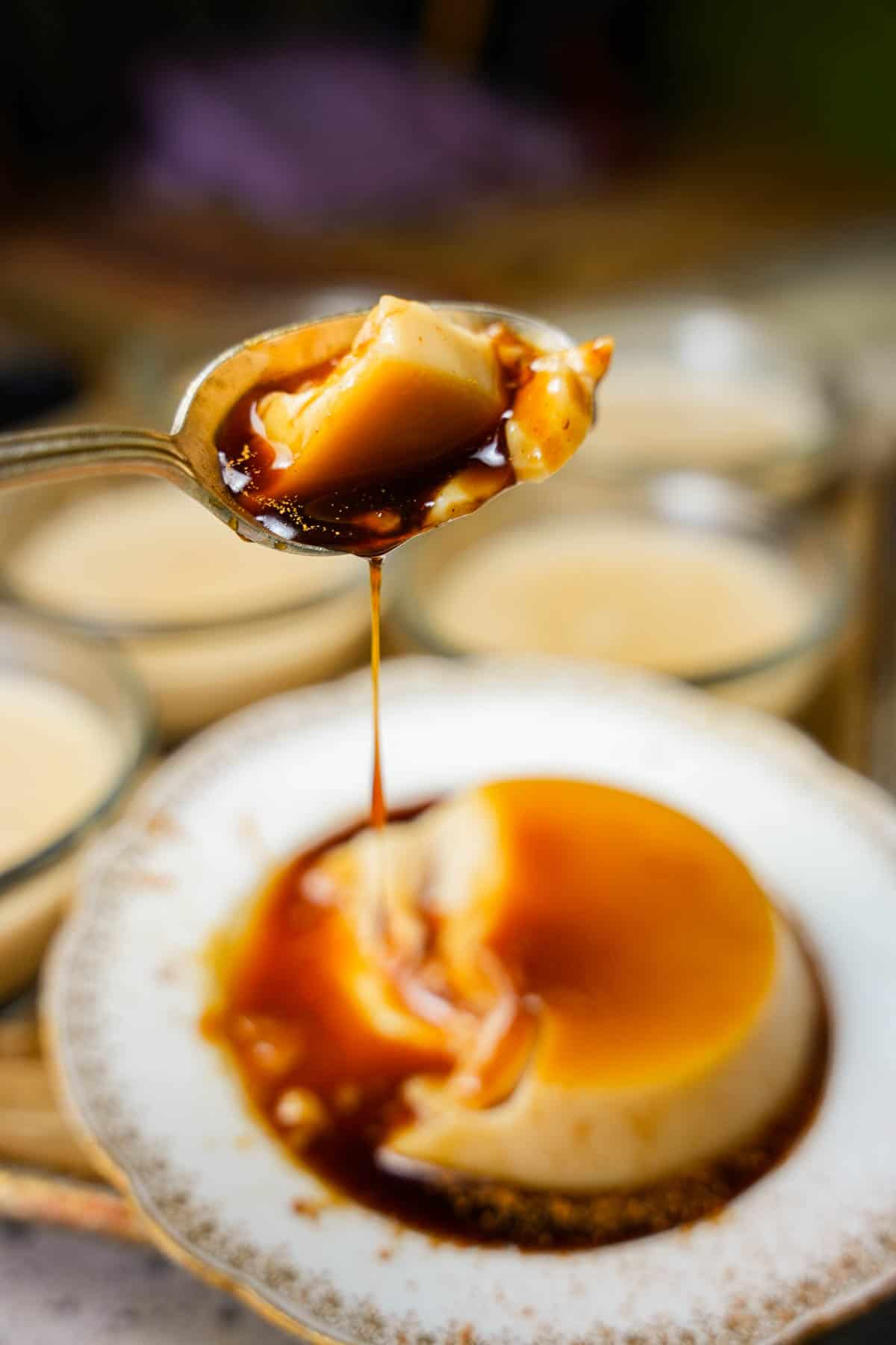 A spoonful of banh flan dripping with caramel is held over a plate with flan.