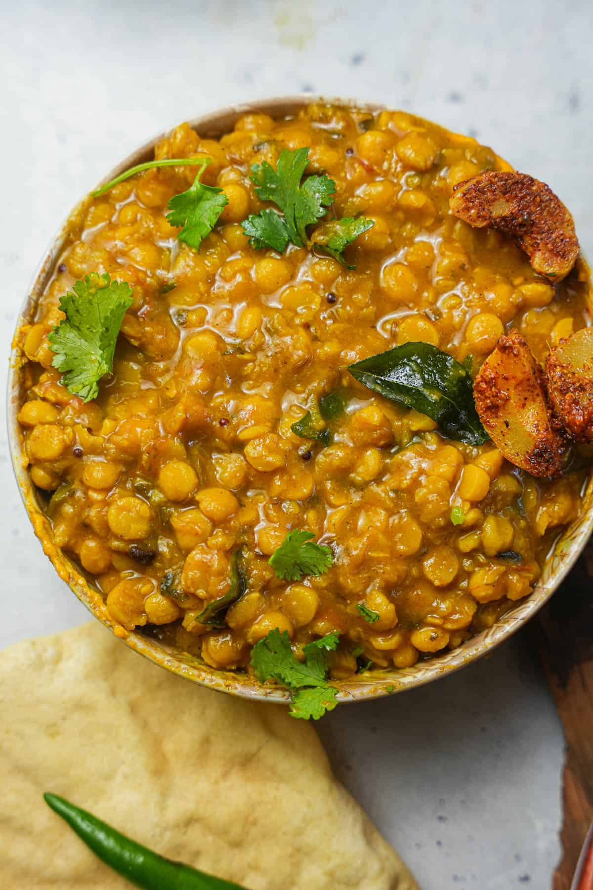 a bowl of chana dal garnished with cilantro with pickled amla on a table with papad.