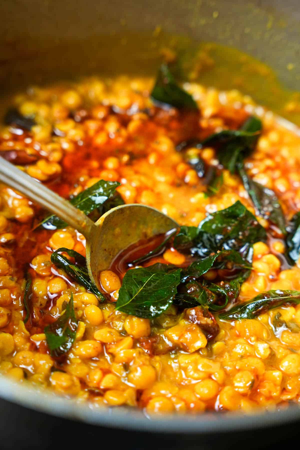 a pot of chana dal having tadka mixed into it. a spoon is shown stirring.