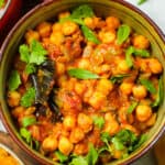 a green ceramic bowl of chana masala with tomatoes and spices garnished with methi and cilantro.