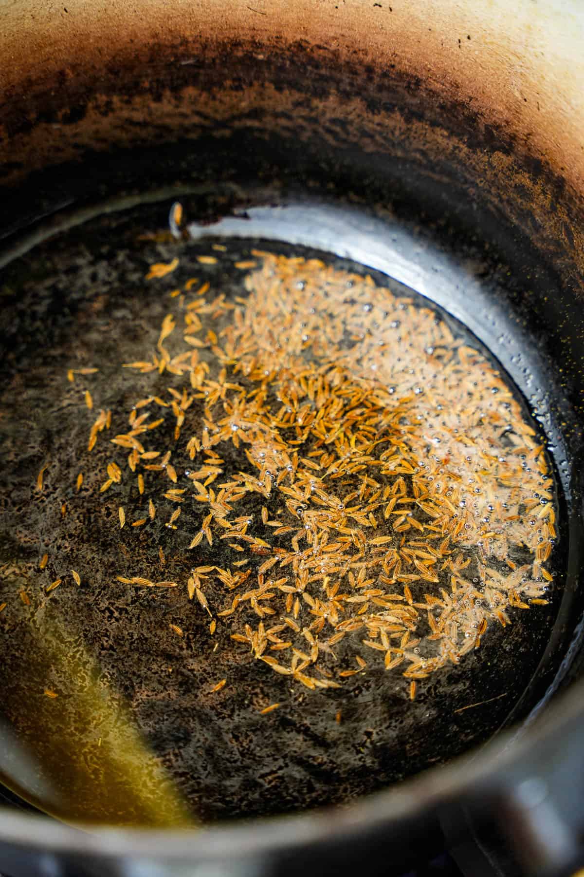 a pan with a cumin seeds frying in hot oil.