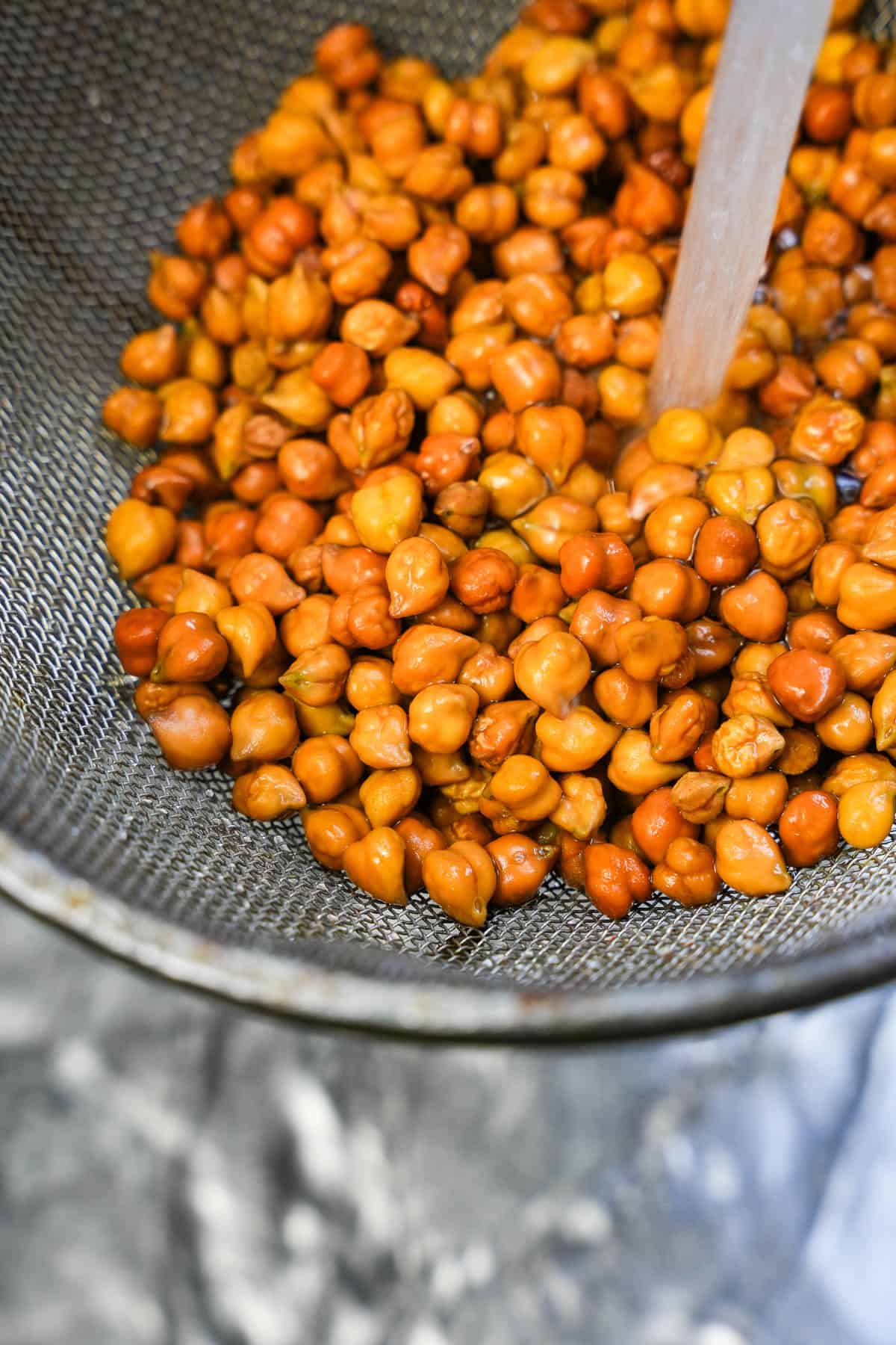 a person pouring liquid into a wire mesh strainer of chana dal to rinse it.