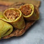 A couple pieces of kuih dadar on a wooden board. One crepe is cut open and you can see the moist coconut filling inside.