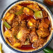 An blue rimmed ceramic bowl full of mango pickle on a table.