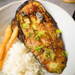 a white bowl of rice with a serving of eggplant and pickled burdock root in it.