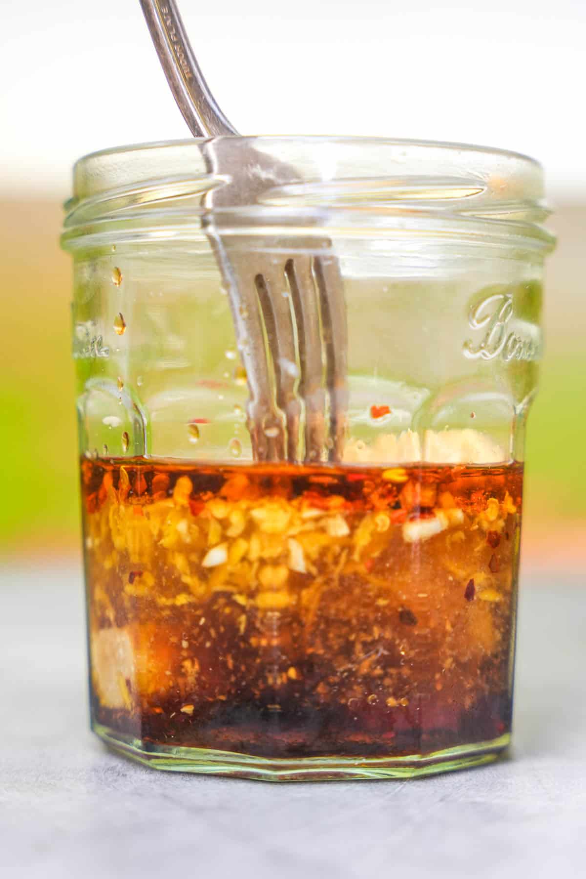 The marinade is mixed with a fork in a glass jar.