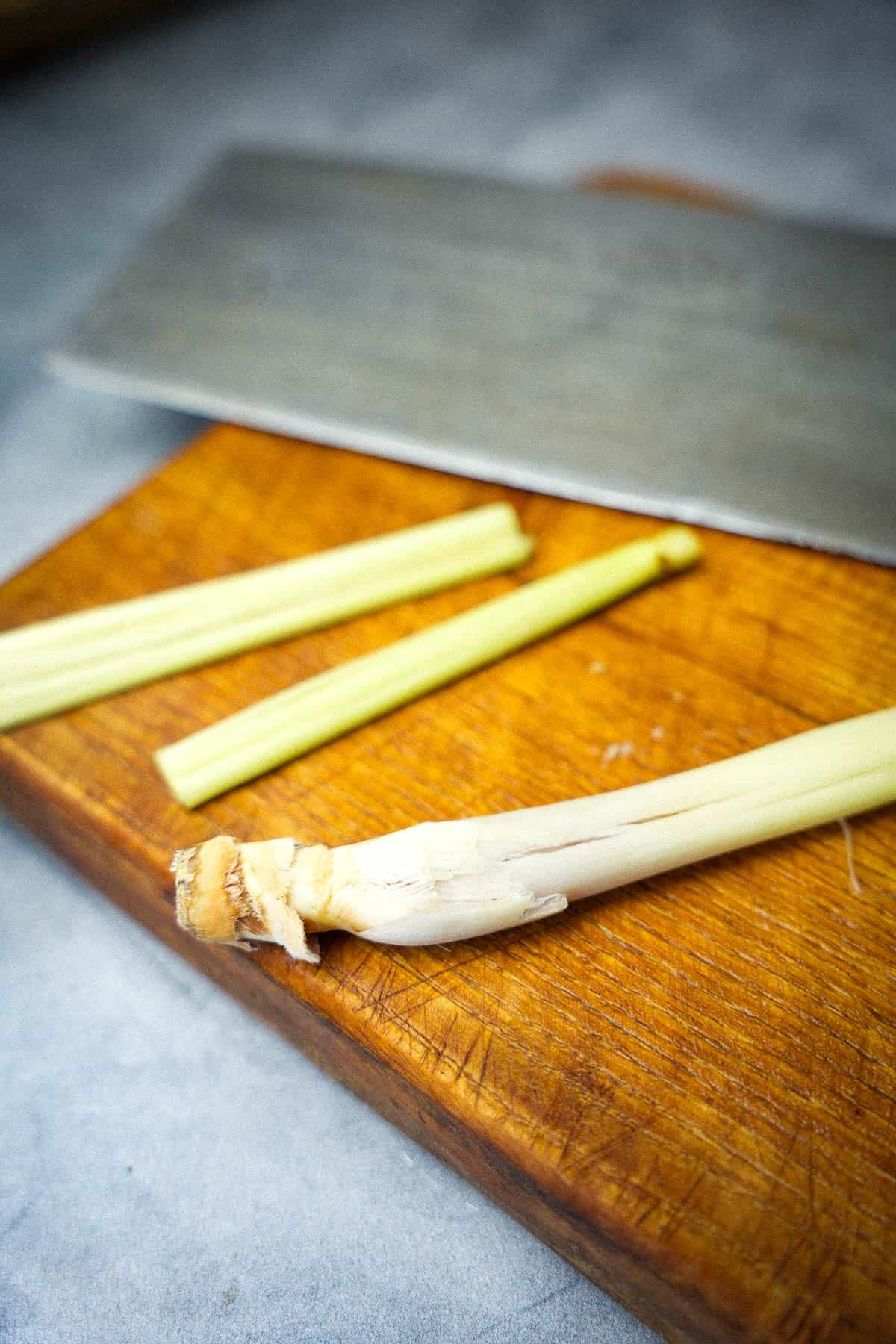 two pieces of lemongrass on a cutting board being crushed with the side of a cleaver..