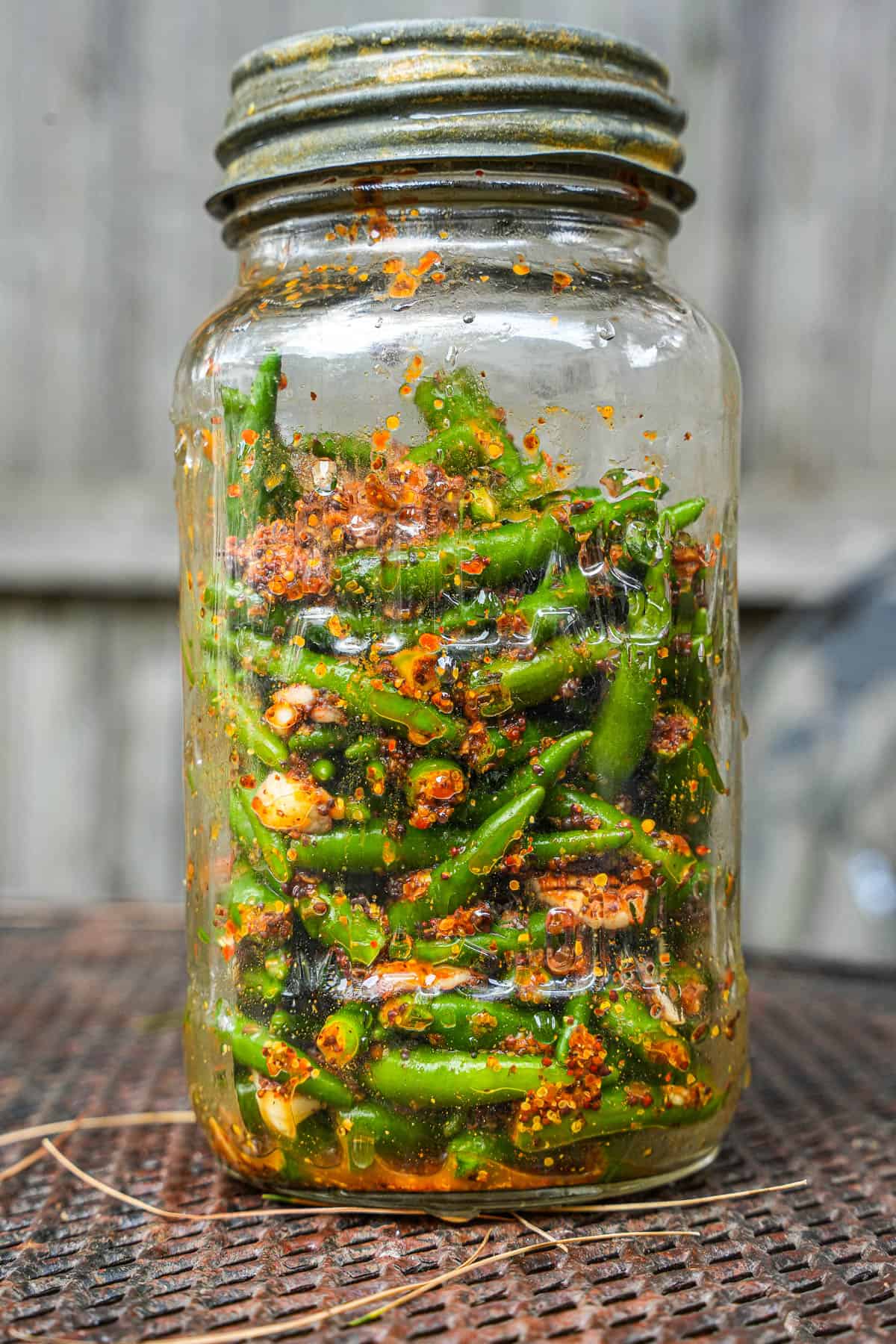 Green chili pickle is fermenting in a glass jar.