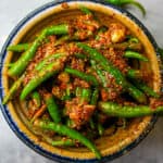 a blue-rimmed ceramic bowl of green chili pickles with spices in it.