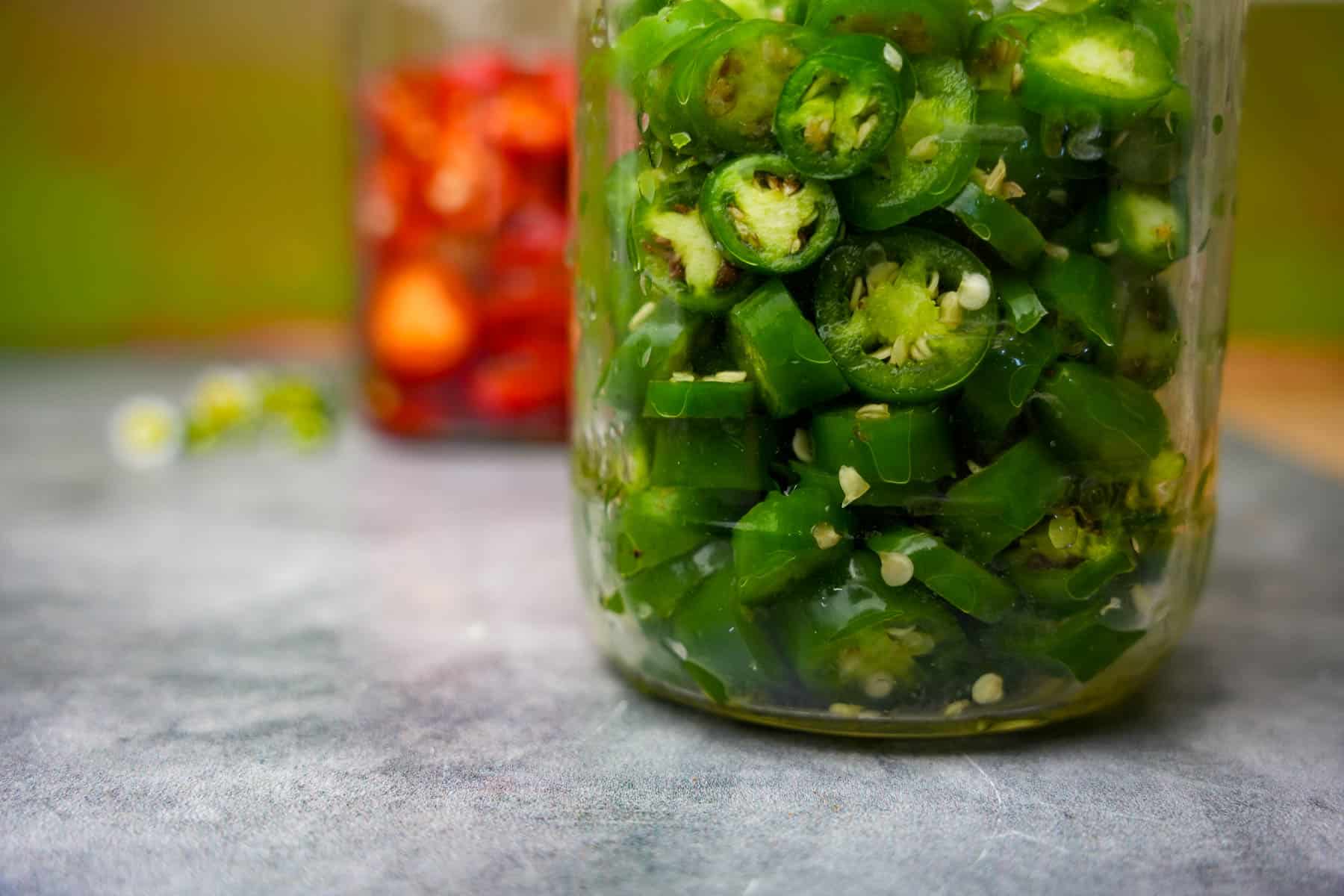 Salted red and green chilies in glass jars before fermentation.