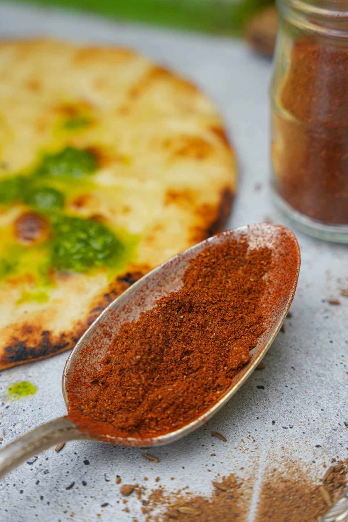 A spoon with baharat on it next to a grilled pita bread with shatta.