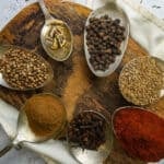 Spices in spoons on a wooden cutting board.