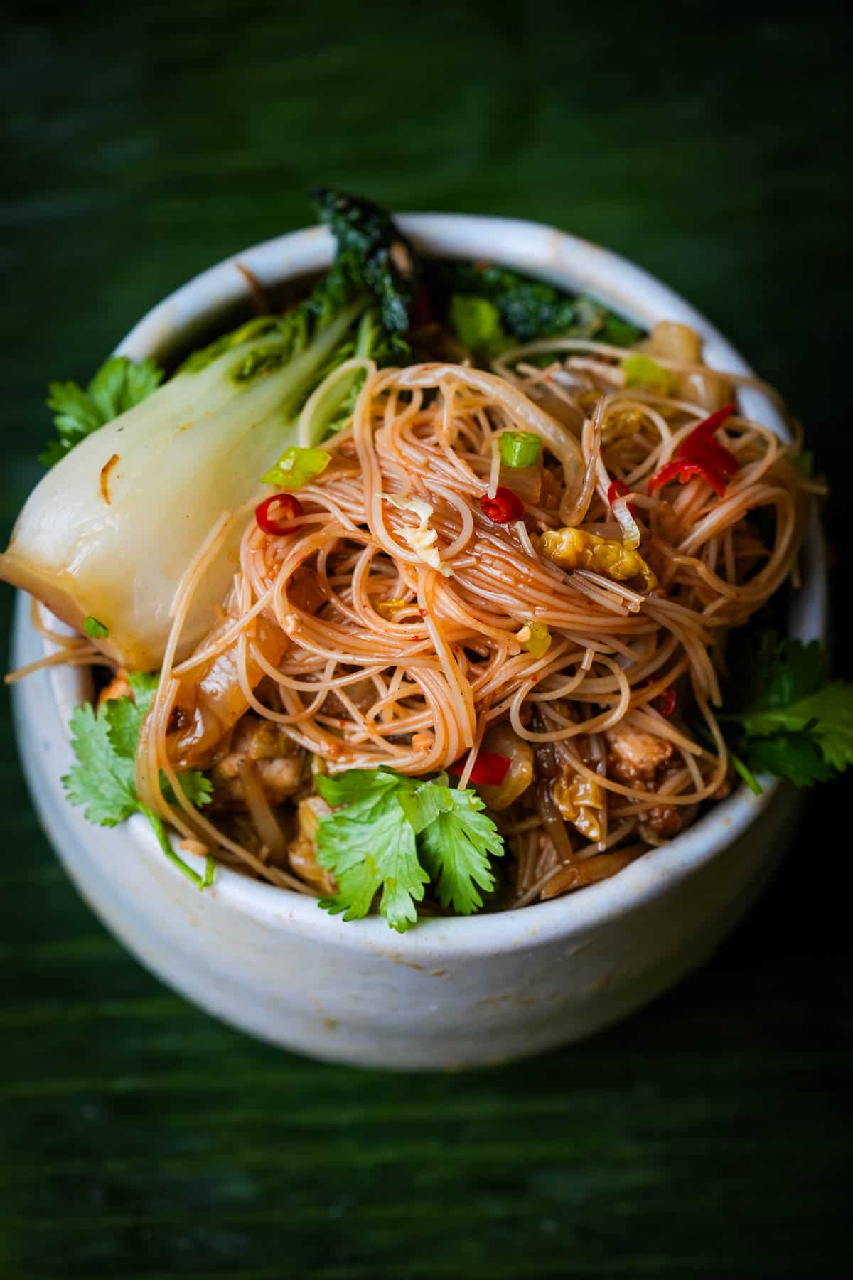 A bowl of noodles with vegetables and herbs.