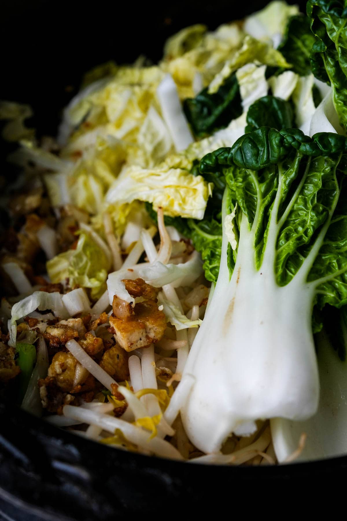 Tofu and vegetables stir frying in a black pot.