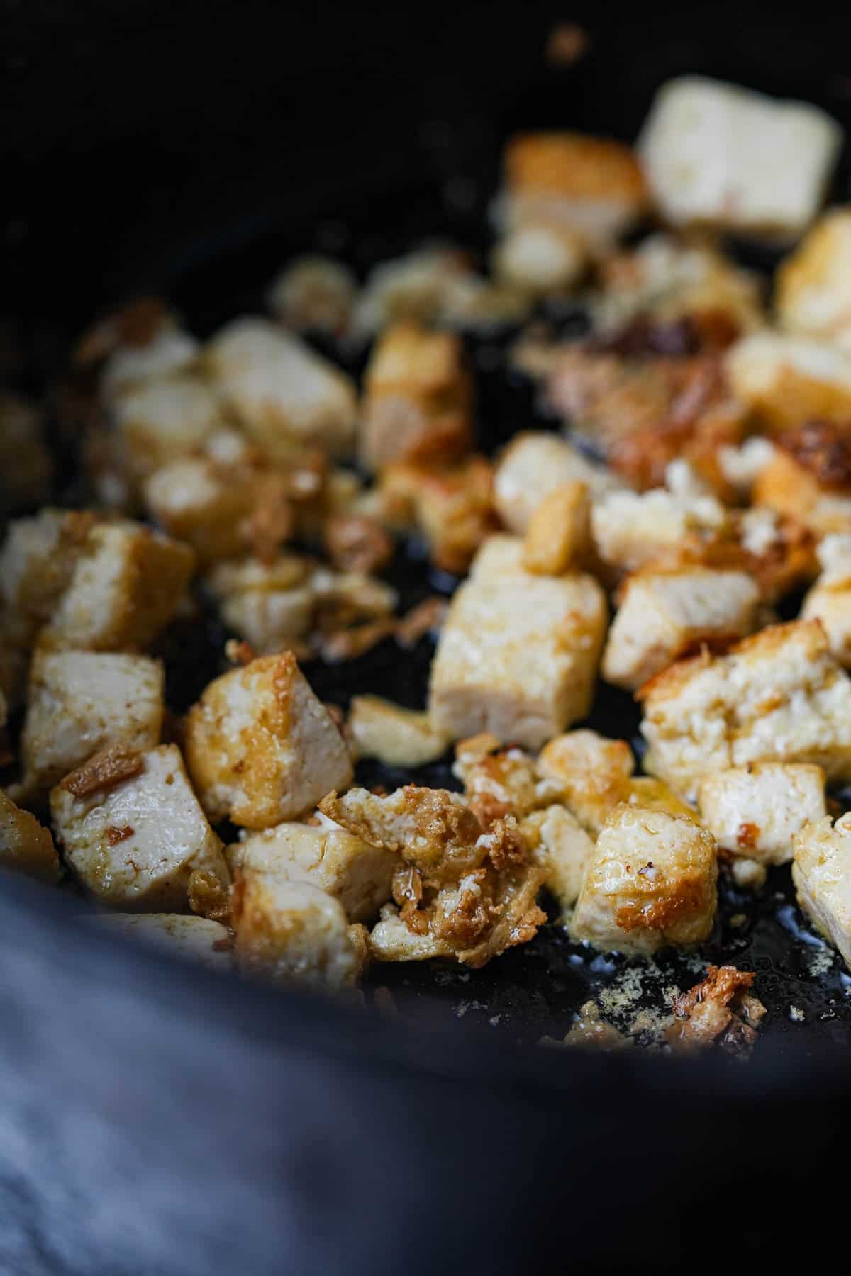 Tofu sauté in a dark colored pan.