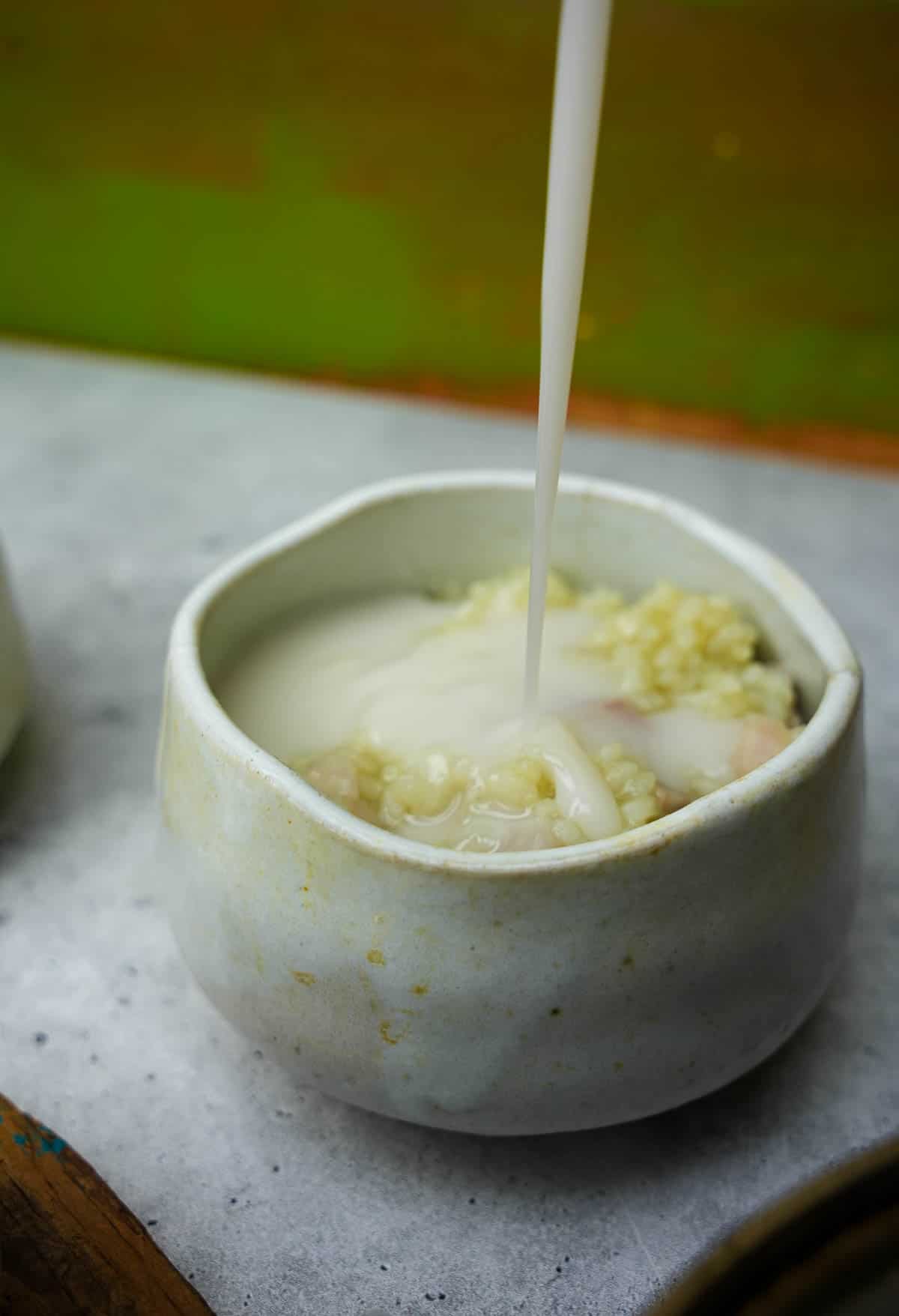 A bowl of taro pudding is having coconut milk topping poured into it.