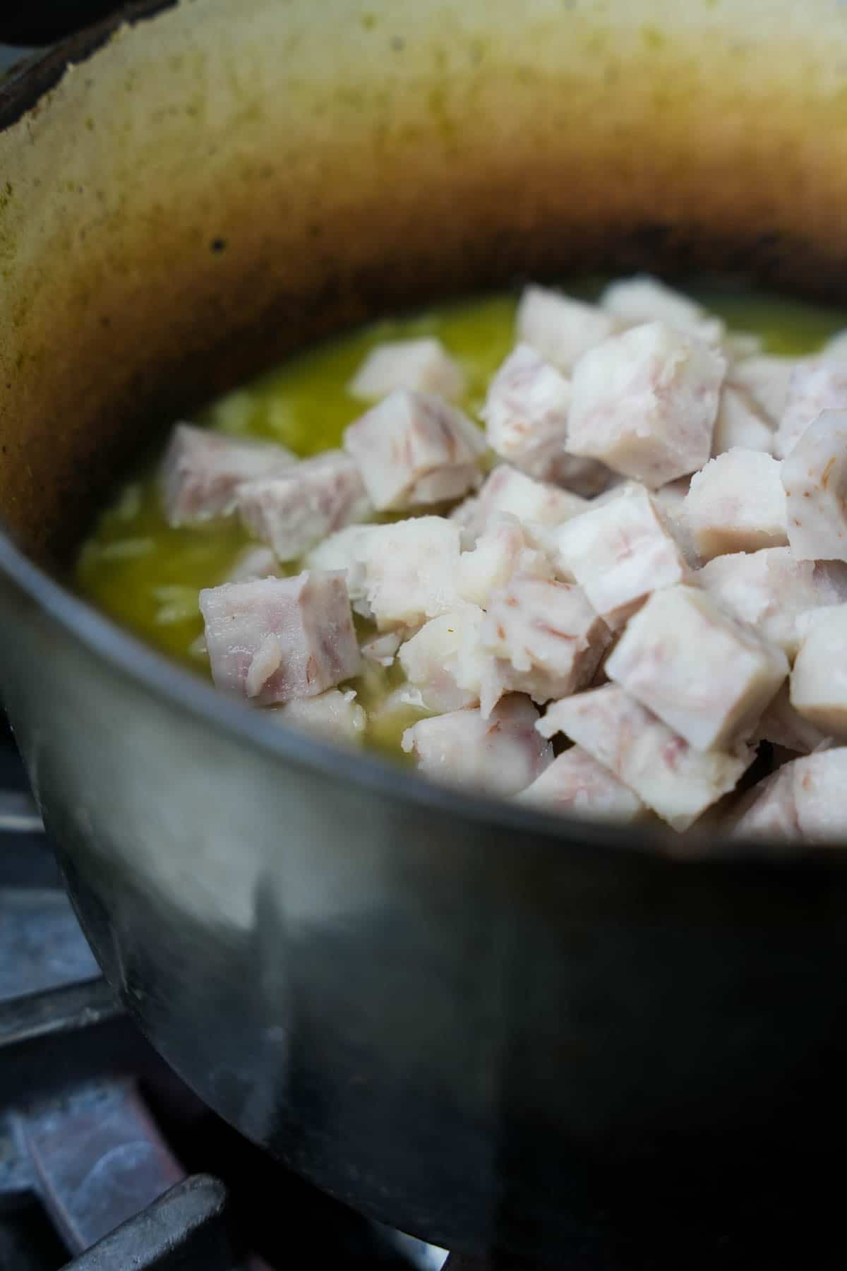 Steamed taro is added to the sweet rice cooking in pandan water in a pot.