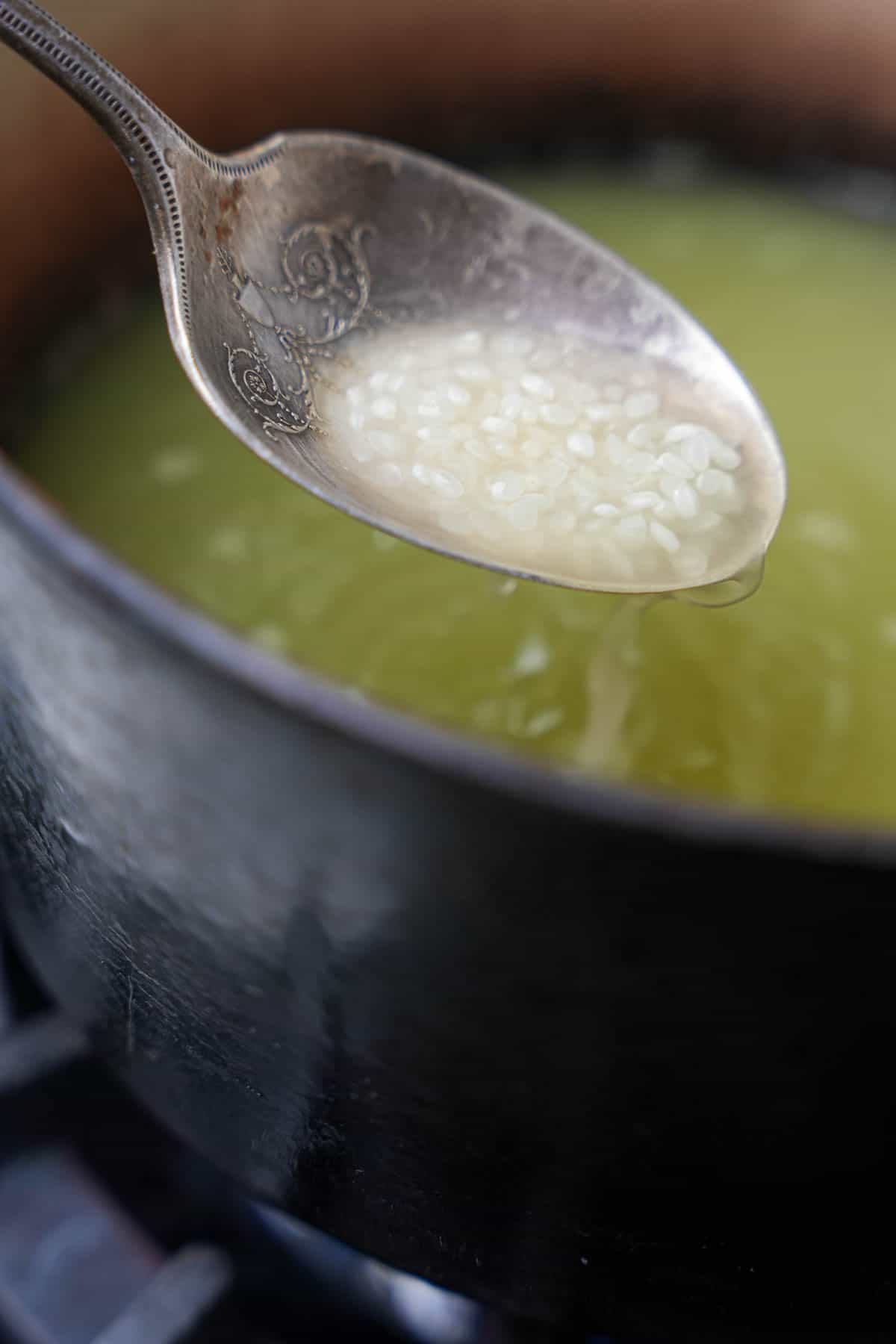 A spoon is stirring a pot of rice and pandan water together.