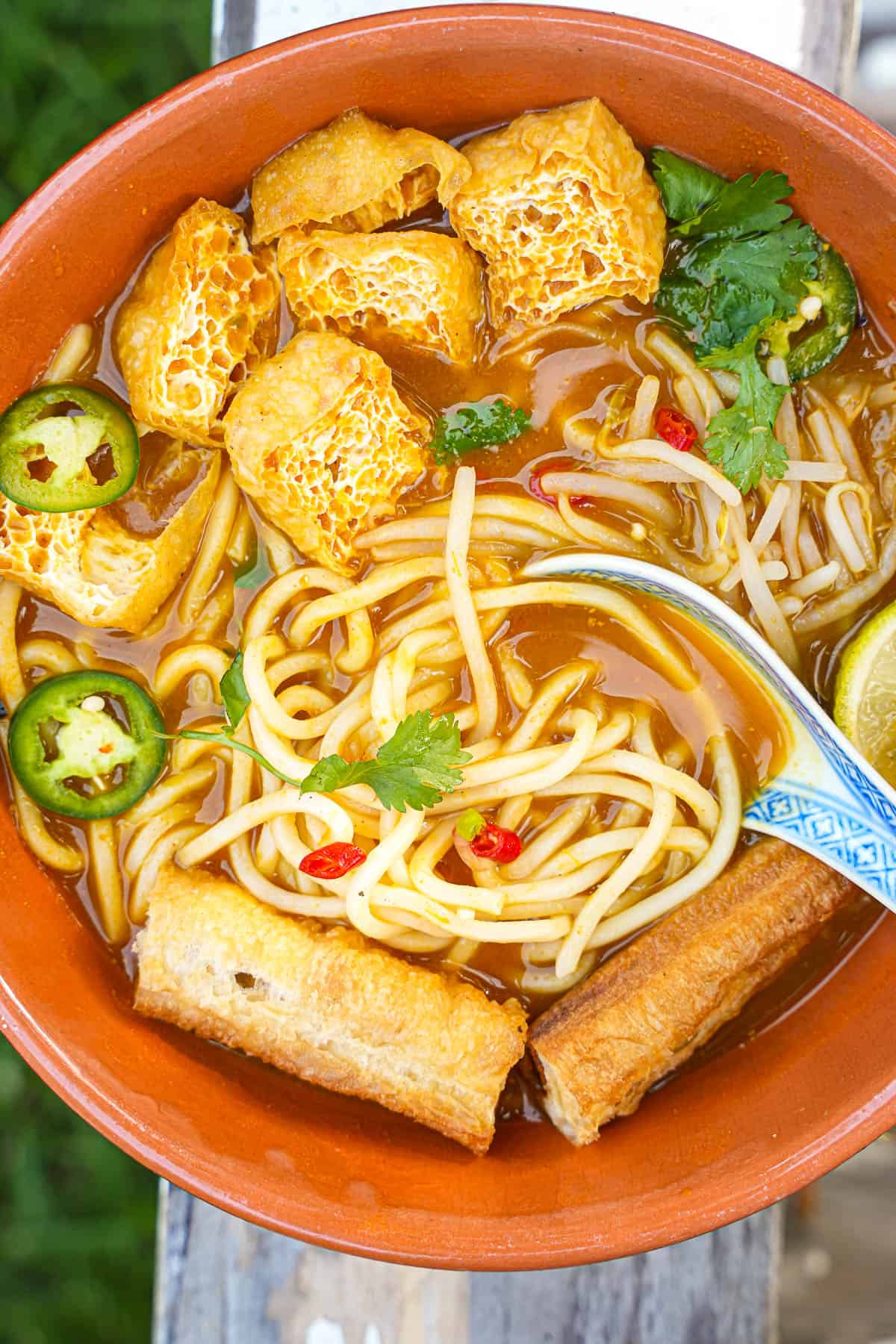 A bowl of mee rebus with tofu and a ceramic soup spoon in it.