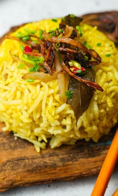 A plate of yellow nasi minyak rice with chopsticks on a wooden cutting board.