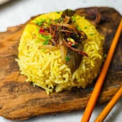 A plate of yellow nasi minyak rice with chopsticks on a wooden cutting board.