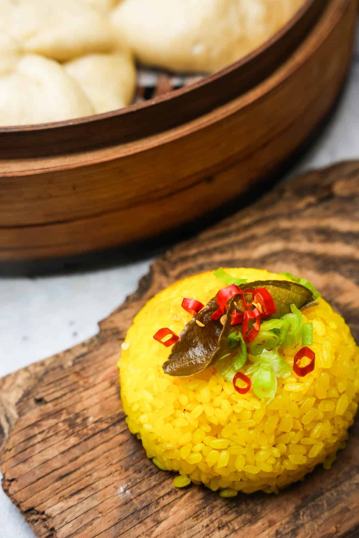 A mount of yellow rice on a wooden board next to a tray of steamed buns.