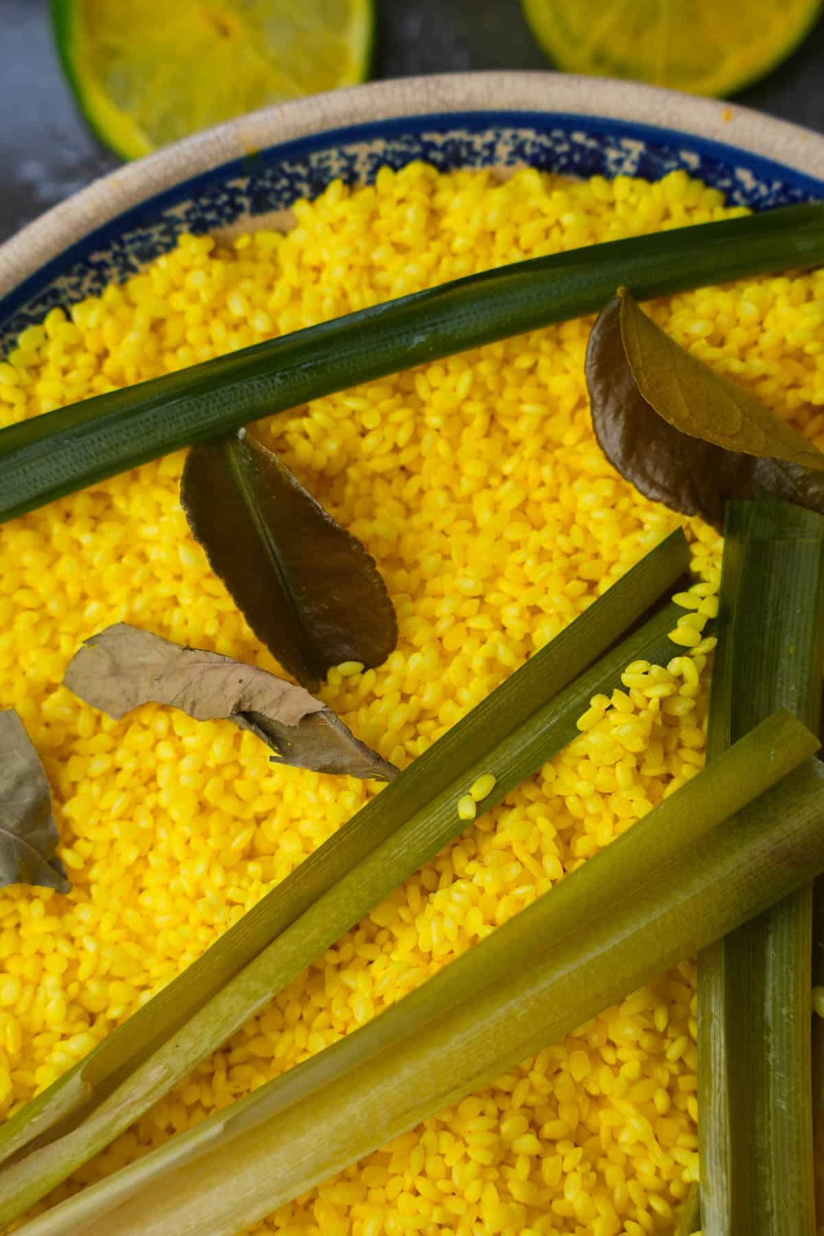 A pie pan filled with yellow rice, pandan and lime leaves.