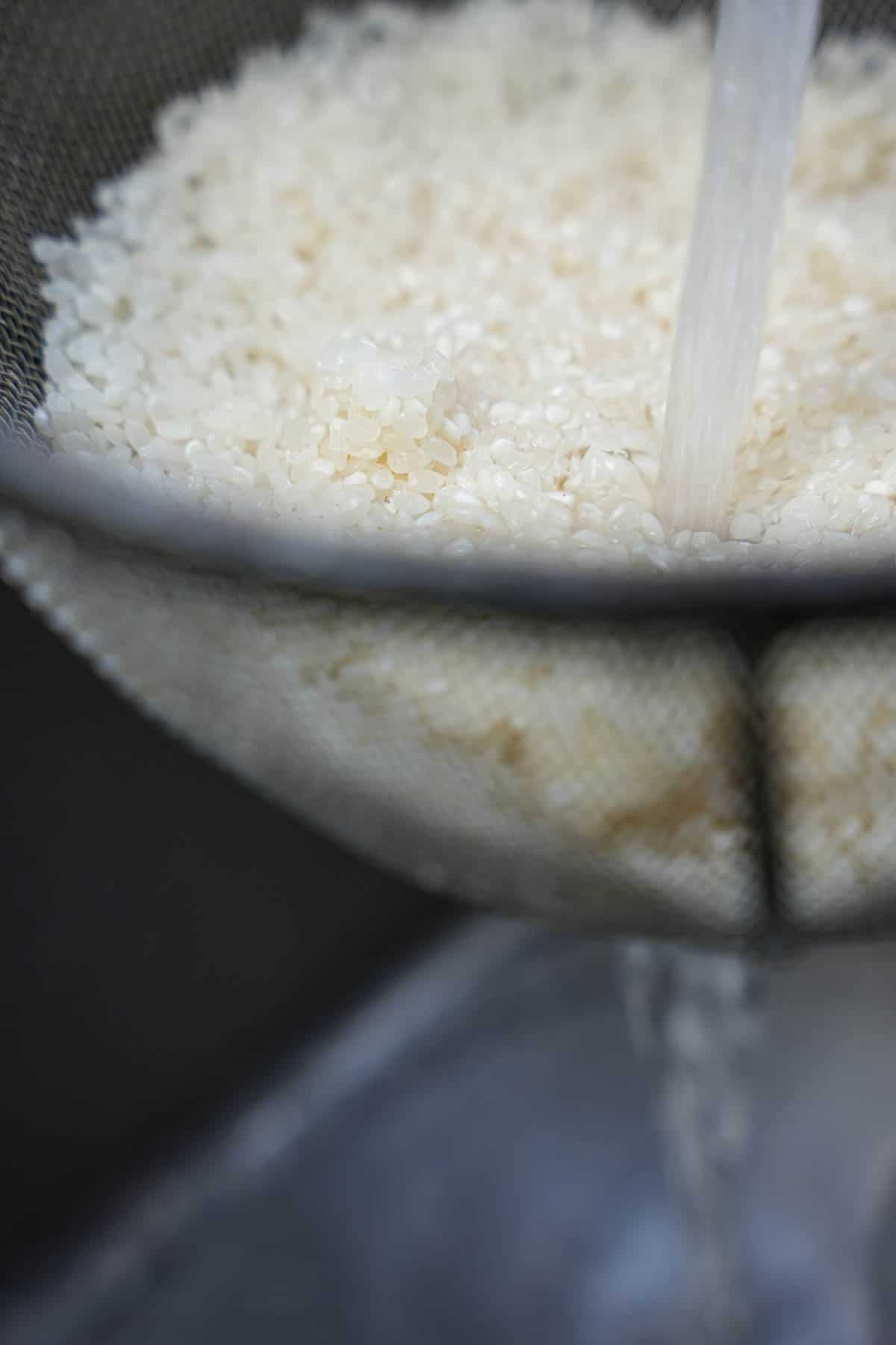 White rice being rinsed in a strainer.
