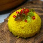 A mound of garnished yellow rice on top of a wooden board.