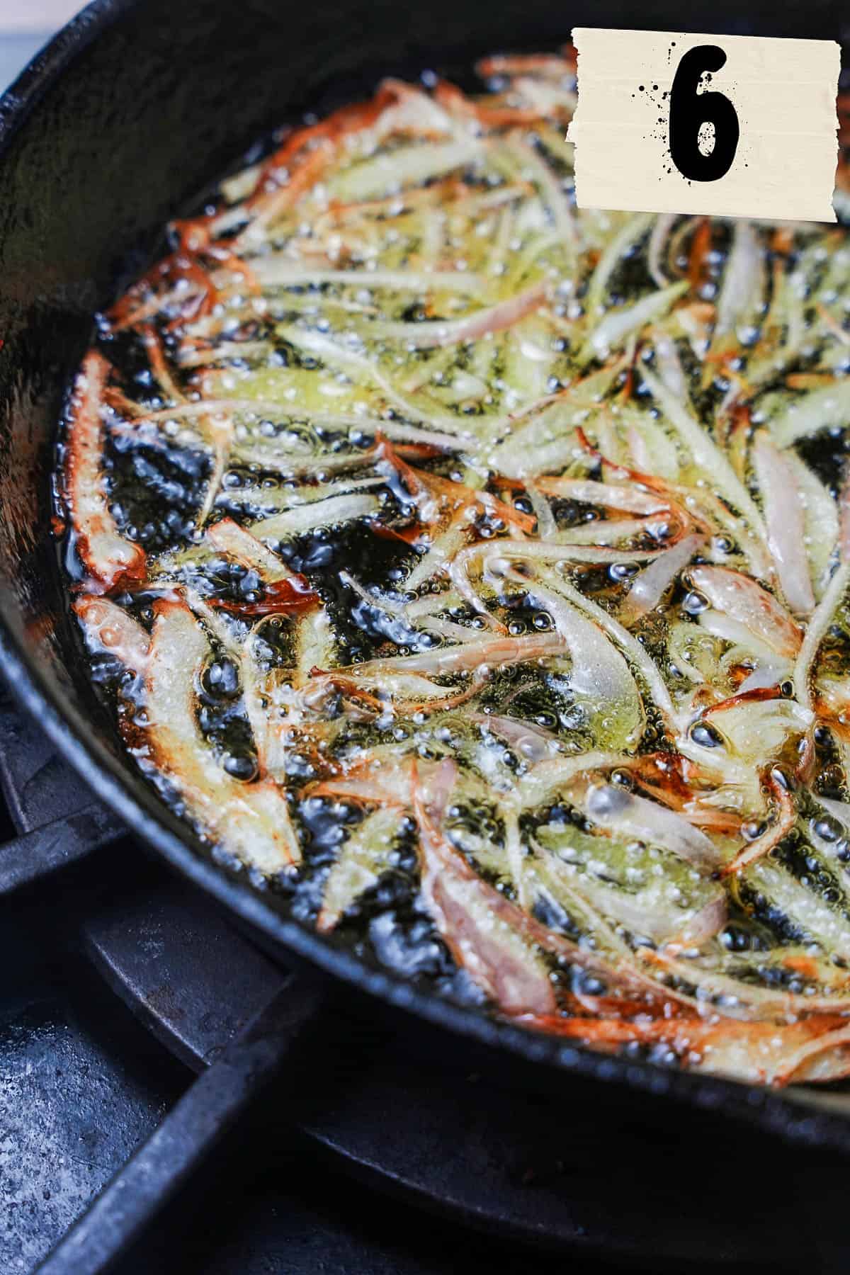 A cast iron pan with shallots frying in it.