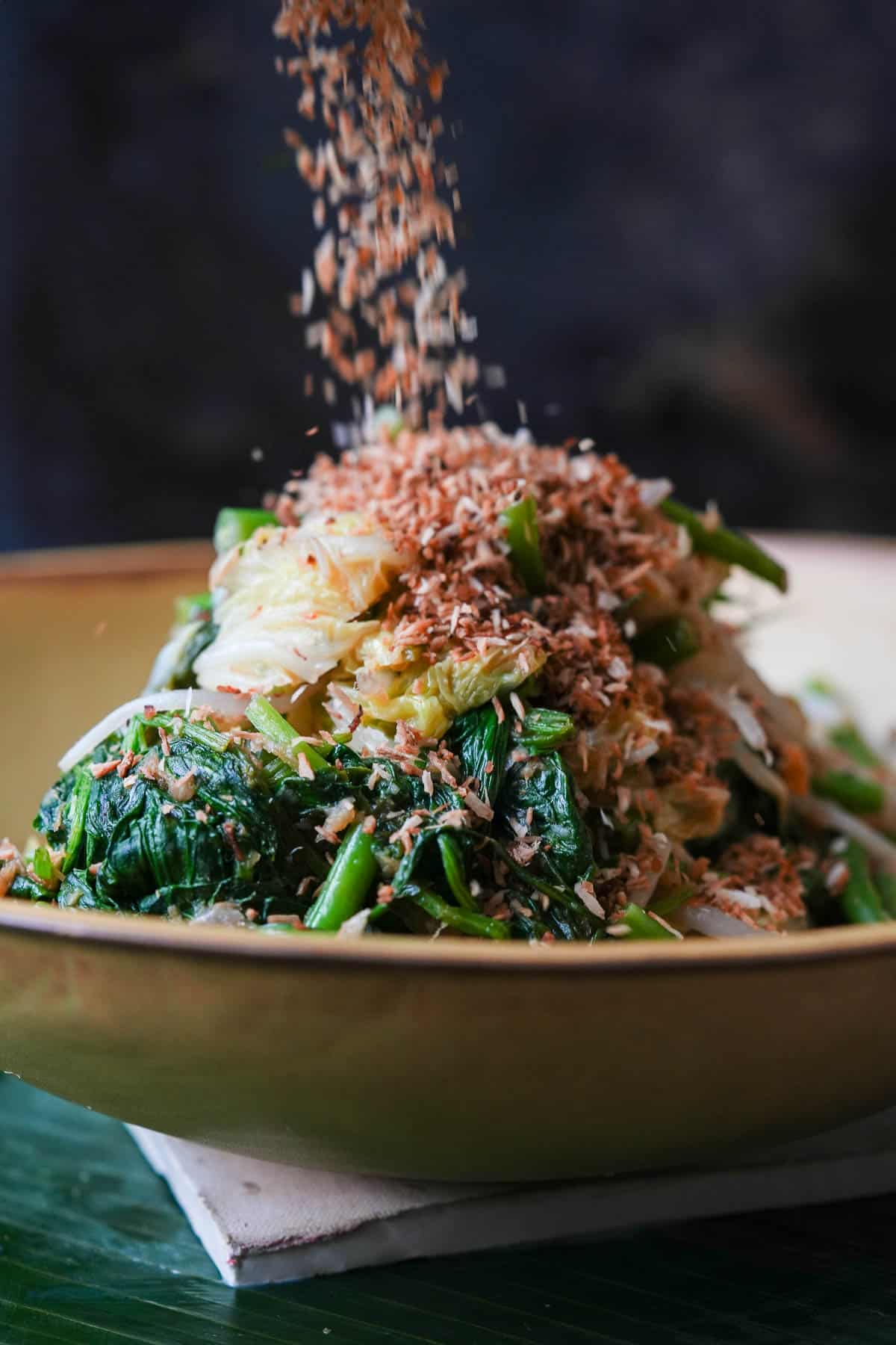 A bowl of Urap Sayur with seasoned toasted coconut sprinkled on top.