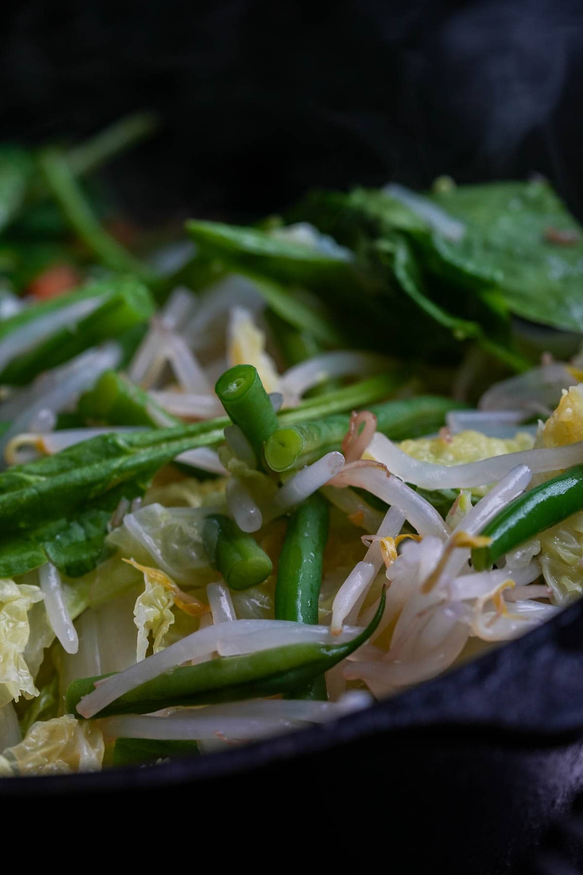 A pan with veggies sauteeing in sambal in it.