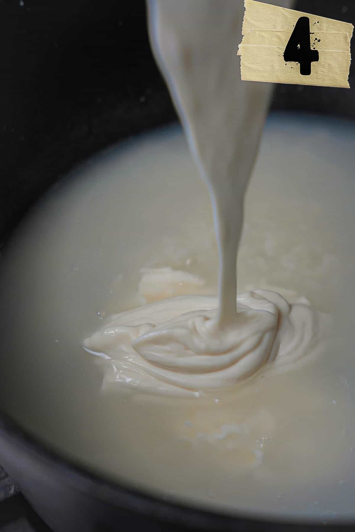 The yogurt mixture is slowly mixed into the cooked rice and water in a dark colored pot.